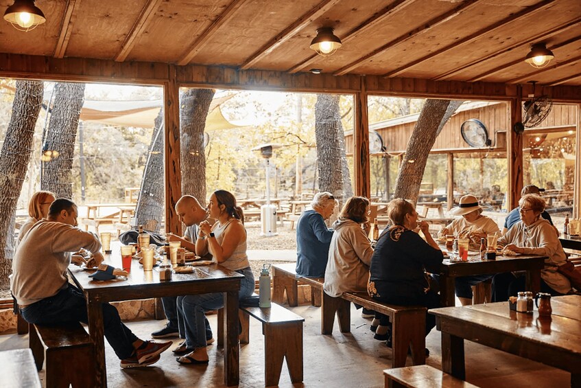 Interior rústico de madera con amplias ventanas, vigas de madera y mesas donde comen personas. 3