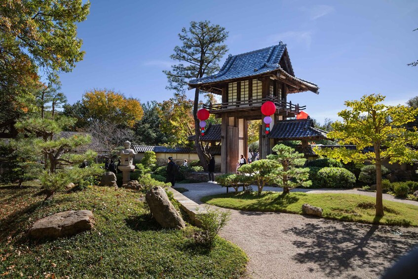 A traditional Japanese building with a tiled roof, surrounded by a well-maintained garden with rocks, trees, and a gravel path. 1