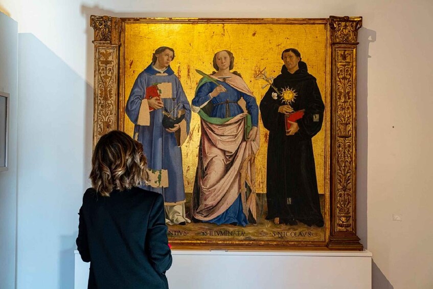 A person viewing a painting with three figures, one holding a book and another holding a staff. 5