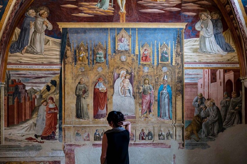 A fresco with religious figures, a central figure in white, and a person observing it. 3