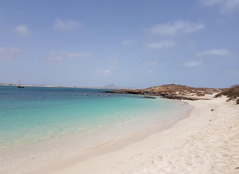 En strand med klart turkis vand, en sandet kystlinje og et fjerntliggende bjerg. 4