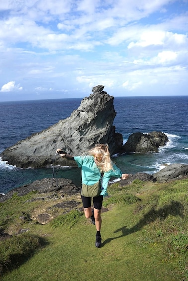 Eine Person wandert auf einer grasbewachsenen Klippe mit Blick auf das Meer und einer großen Felsformation. 1
