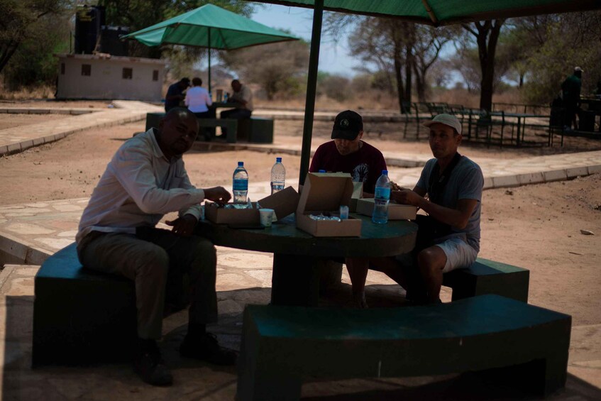 Tres hombres sentados a una mesa con una computadora portátil, botellas de agua y una caja. 5