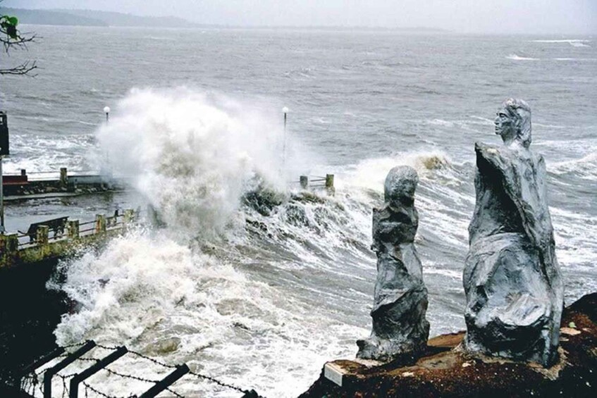 A stormy sea with waves crashing against a rocky shore, two stone statues, and a distant shoreline. 5
