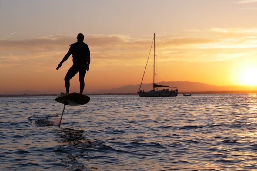 A person surfing on a board, a sailboat, and a sunset over the ocean. 1
