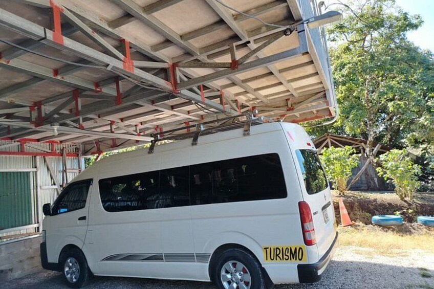A white van parked under a covered area with a 'TURISMO' sign on the side. 1