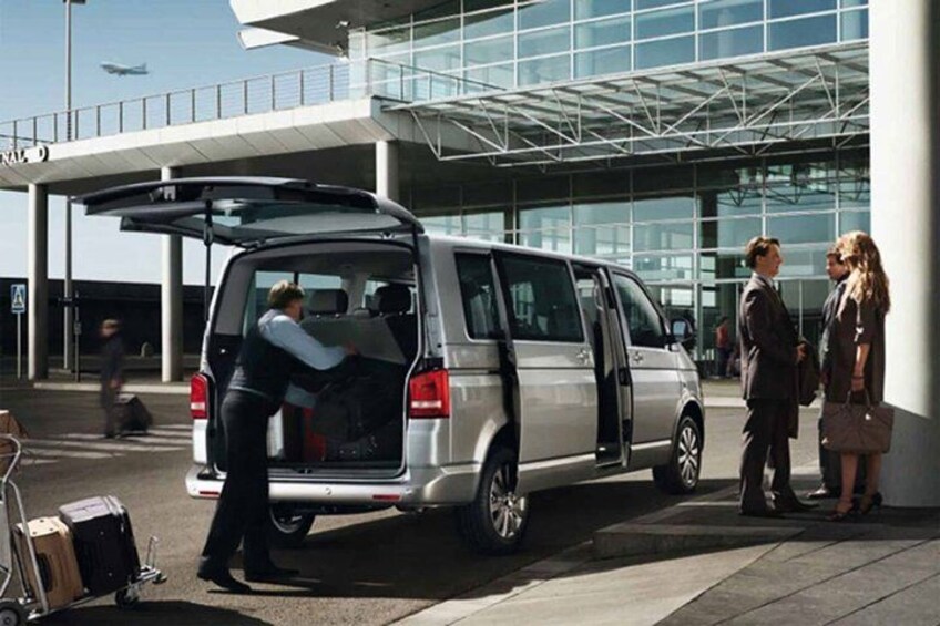 A silver van with its door open, luggage on the ground, and people standing nearby. 3