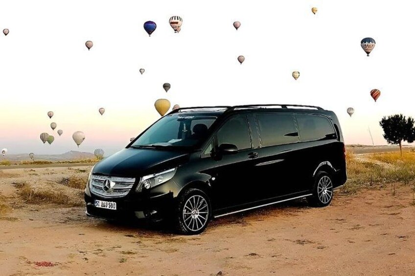A black SUV parked on a dirt road with hot air balloons in the background. 2