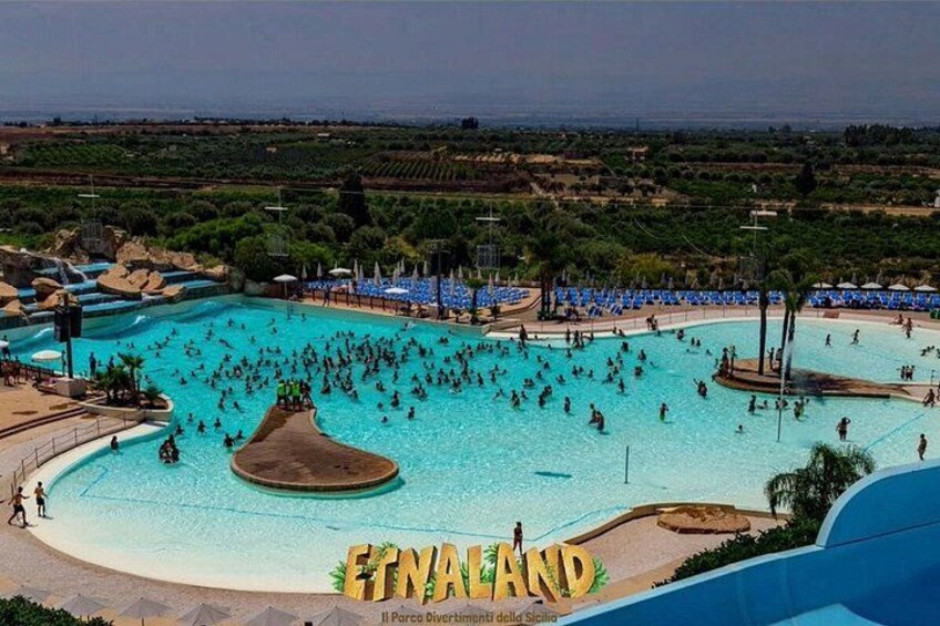 A large outdoor swimming pool with people swimming and sunbathing, surrounded by beach chairs and umbrellas. 4