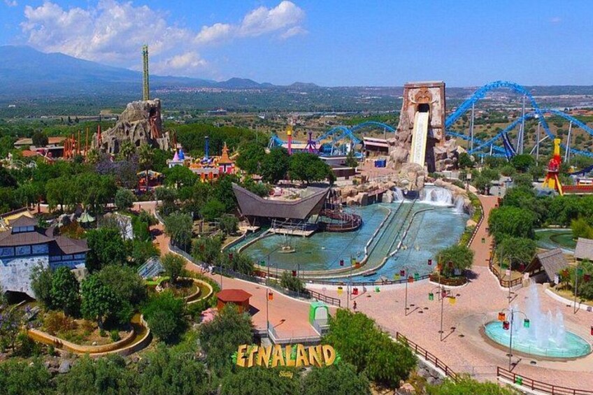 A theme park with a large water slide, roller coasters, and a mountainous landscape in the background. 1