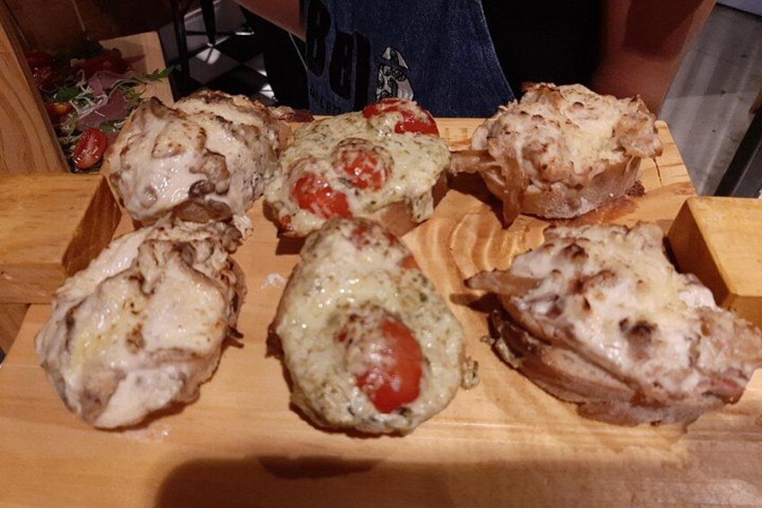 A wooden board with several baked items, possibly savory pastries or small pies, with visible fillings like cheese and tomatoes. 2