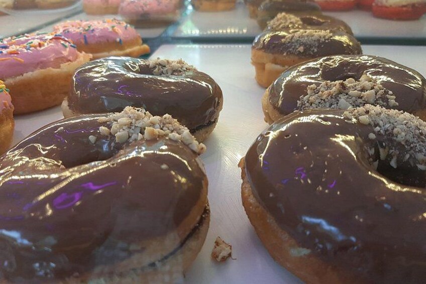 A variety of donuts with chocolate and pink icing, some topped with nuts. 5