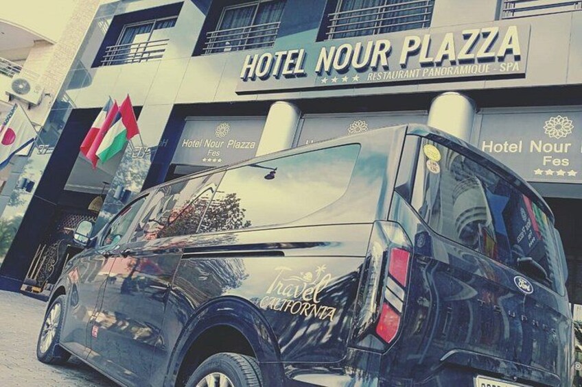 A black van parked in front of Hotel Nour Plaza with a sign that reads 'Hotel Nour Plaza Restaurant Panoramaque Spa.' 2