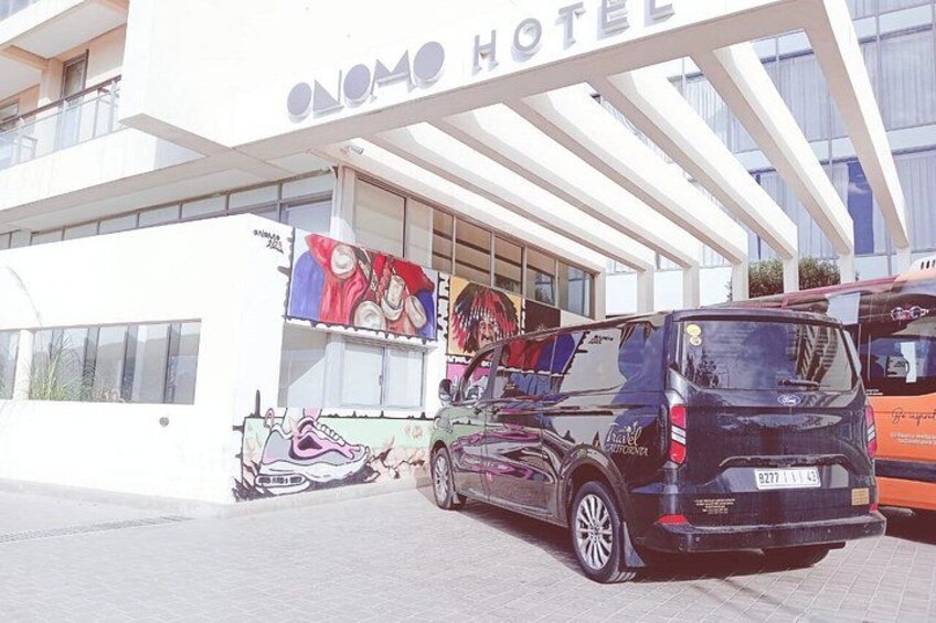 A hotel with a colorful mural on the side, a black van parked in front, and a bus in the background. 4