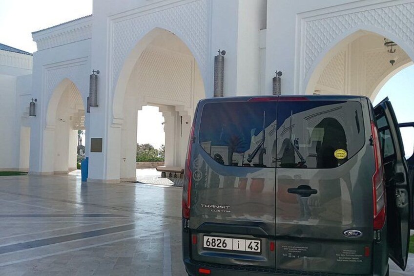 A dark-colored van parked in front of a white building with large arches. 5