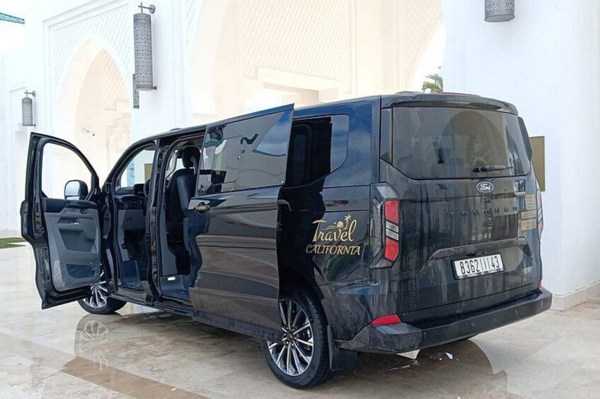 A black van parked in front of a white building with an open door. 1
