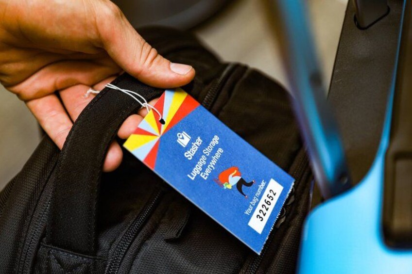 A hand holding a luggage tag with a colorful design and text. 1