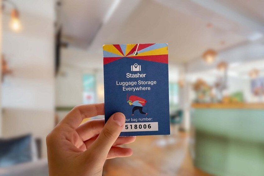 A hand holding a blue card with a luggage storage service logo and a luggage tag number. 3