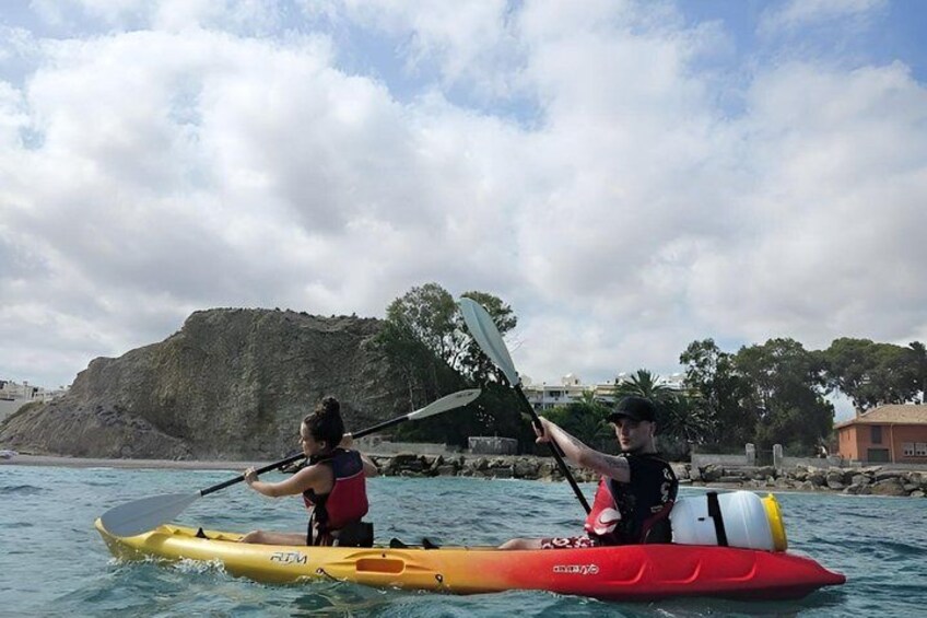 Two people kayaking on a calm body of water with a rocky outcrop in the background. 3