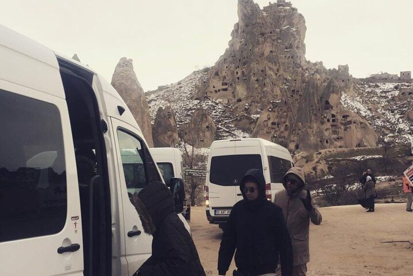 A group of people near white vans with a rocky, mountainous background. 3