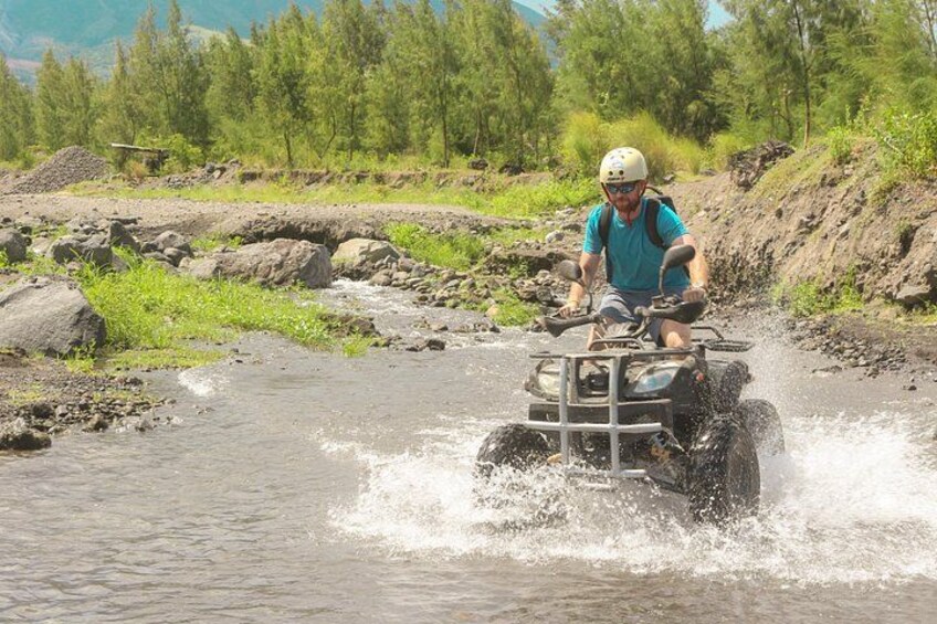 A person riding an ATV through a shallow river. 2