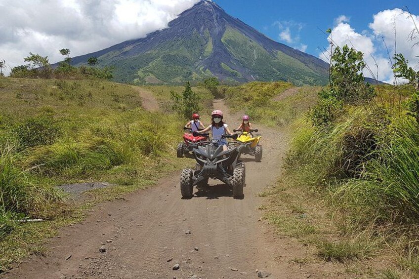 Two people on ATVs on a dirt road with a volcano in the background. 5