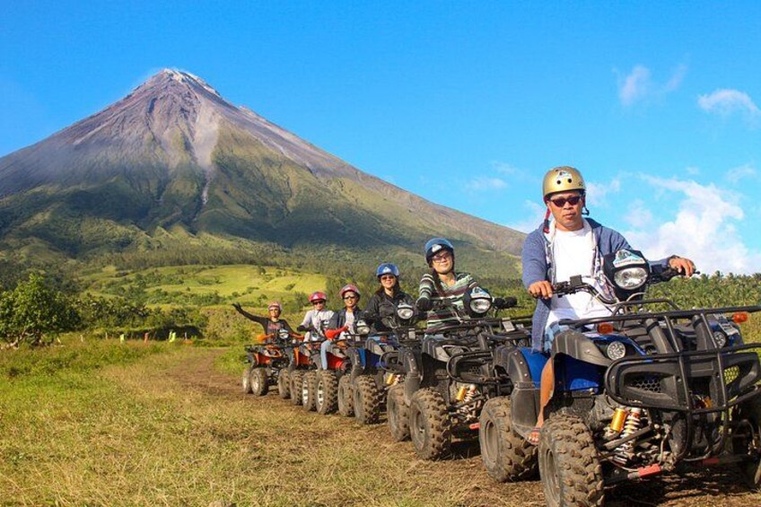 A group of people on ATVs in a grassy field with a volcano in the background. 3