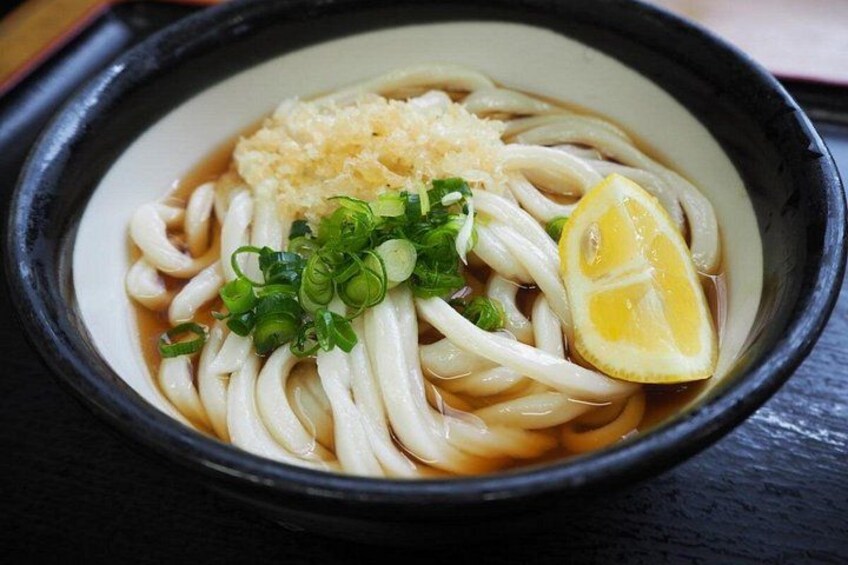 A bowl of ramen with noodles, a slice of lemon, chopped green onions, and a topping of grated garlic. 3