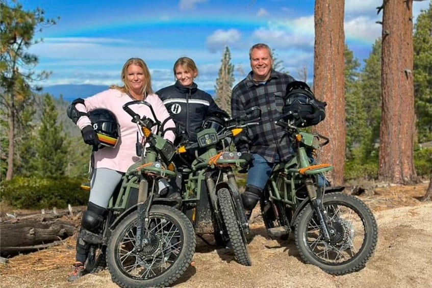 Tres personas en bicicletas de montaña con cascos, de pie en un sendero de tierra con árboles y un cielo despejado al fondo. 3
