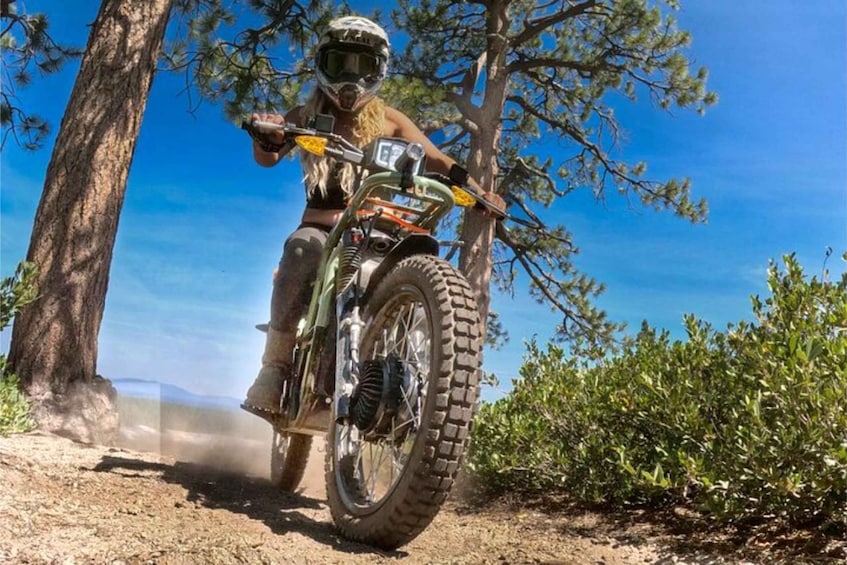 Una persona montando una moto de cross por un sendero rodeado de árboles y arbustos. 1