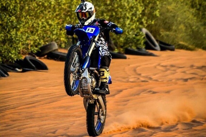 A motorcycle with the number 13 on the side, performing a wheelie on a dirt track. 2