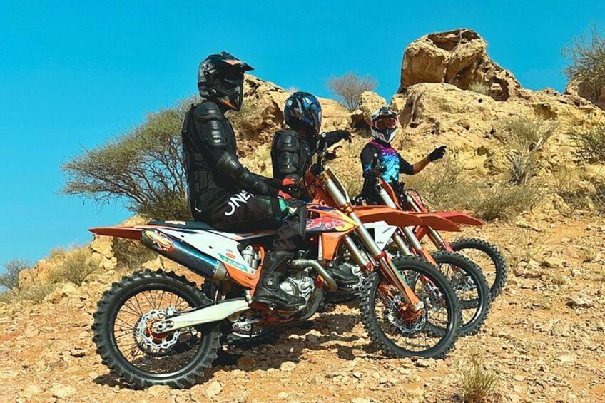 Two riders on off-road motorcycles in a rocky, arid landscape with sparse vegetation. 4