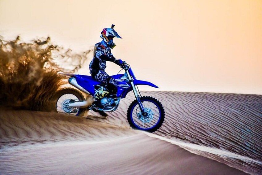 A person riding a blue dirt bike on a sandy dune. 1