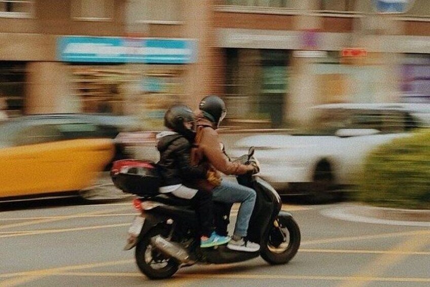 A motorbike with two riders, one adult and one child, on a city street. 2