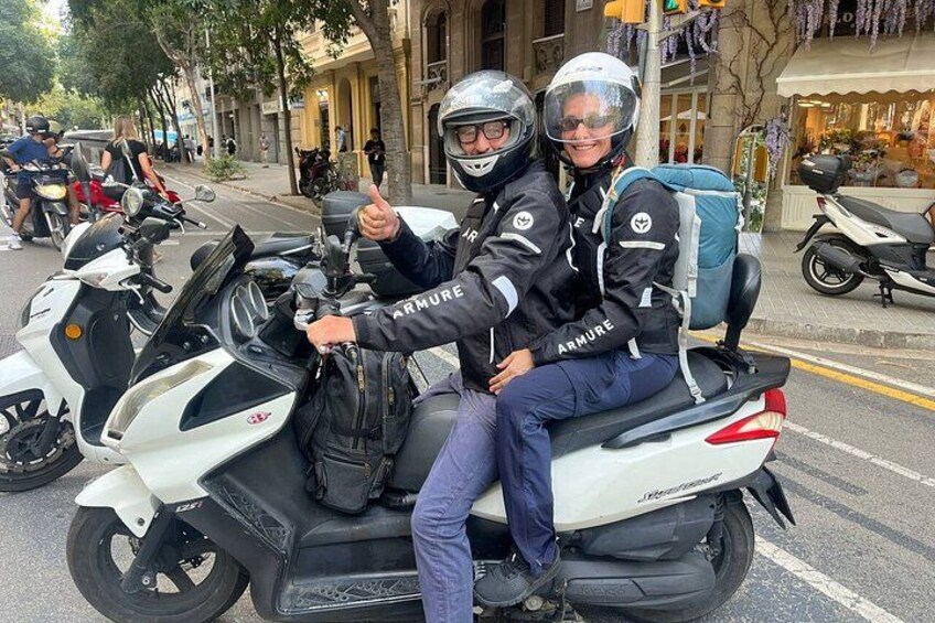 Two people on a white motorcycle with a blue bag, giving a thumbs up. 4