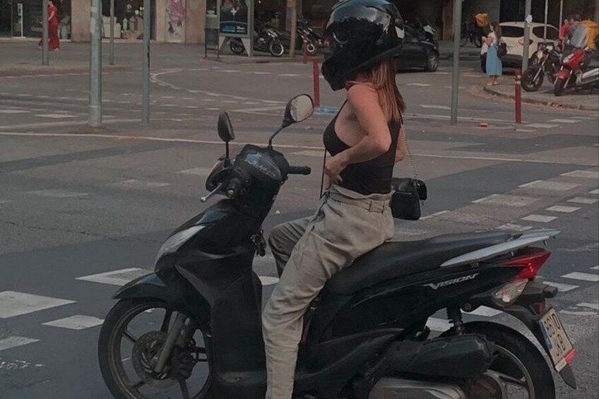 A person standing on a scooter in an urban setting with buildings and a crosswalk in the background. 3