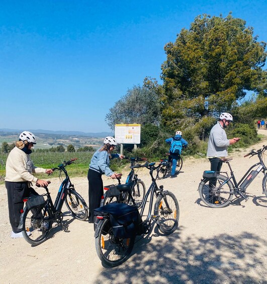 Un grupo de personas con bicicletas y bicicletas eléctricas en un sendero de tierra, con un letrero y árboles al fondo. 4