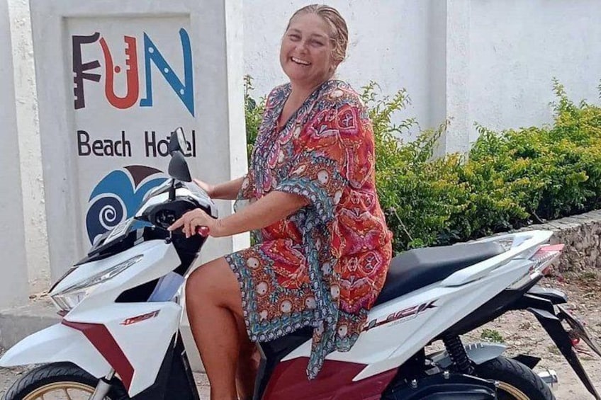 A person sitting on a scooter in front of a building with a sign that reads 'FUN Beach Hotel'. 5