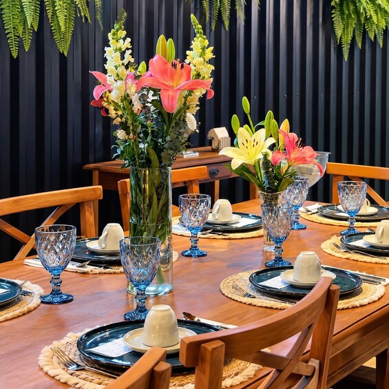 A dining table set with blue glassware, white plates, and a centerpiece of pink and yellow flowers. 2