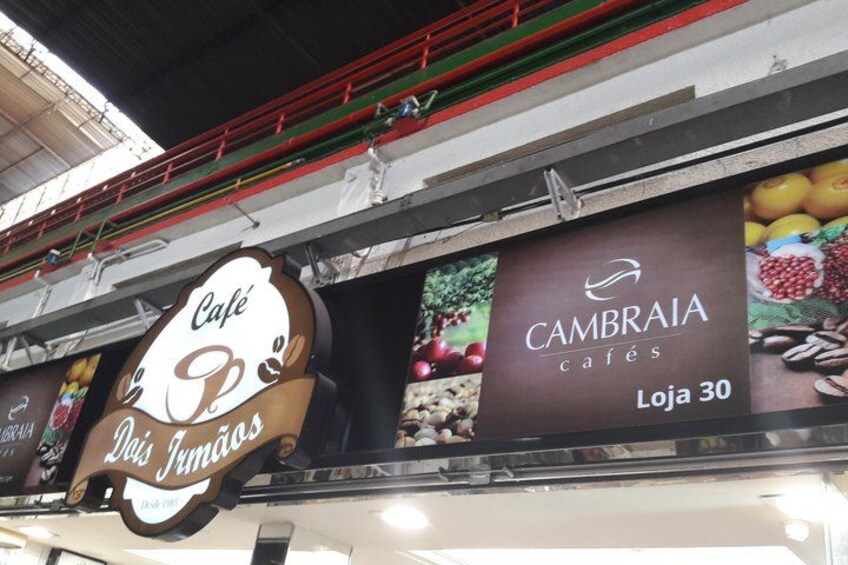 A café named 'Café Dois Jumanos' with a sign featuring coffee beans and fruits. 4