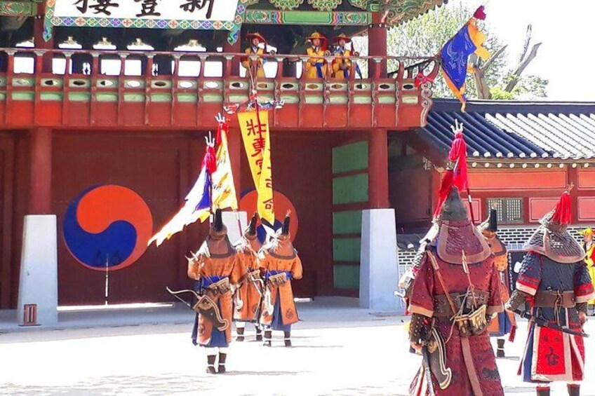 A traditional ceremony with participants in colorful attire, a large emblem, and flags. 5