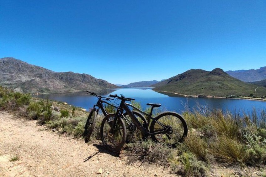 A mountain bike parked on a dirt path overlooking a lake with mountains in the background. 1