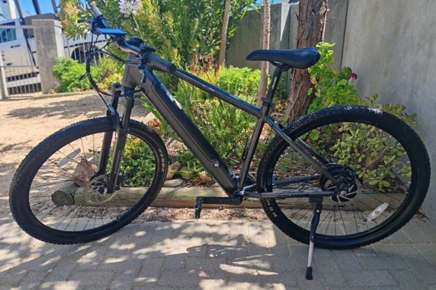 A mountain bike parked on a paved surface with greenery in the background. 4