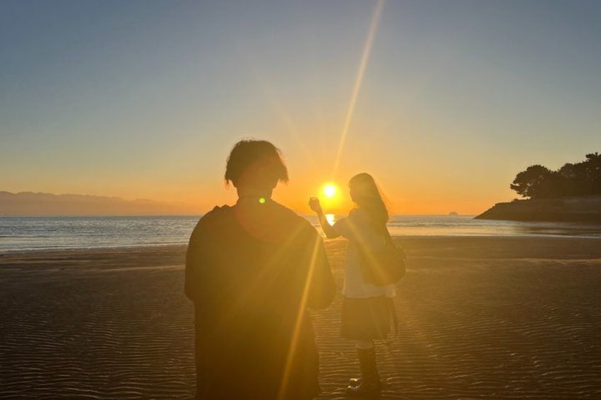 A sunset over a beach with two people silhouetted against the sun. 2
