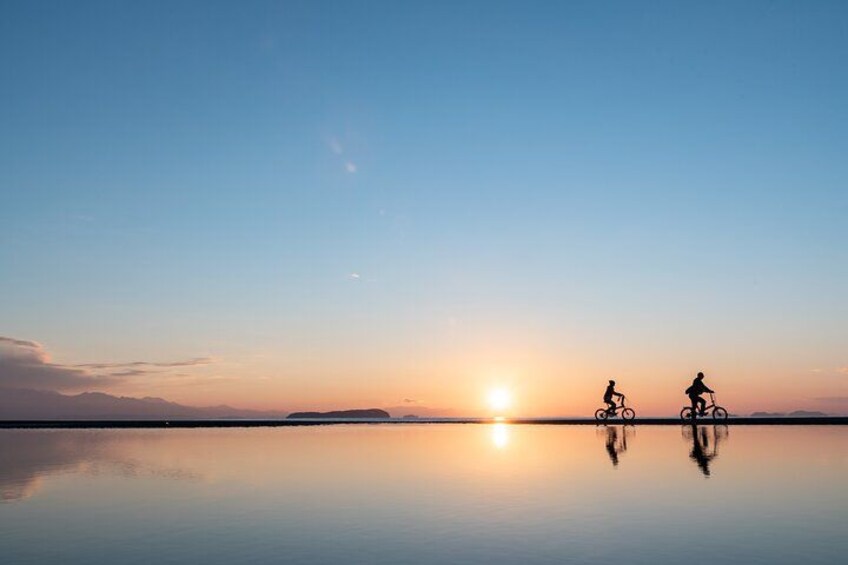 A sunset over a calm body of water with two cyclists silhouetted against the sky. 4