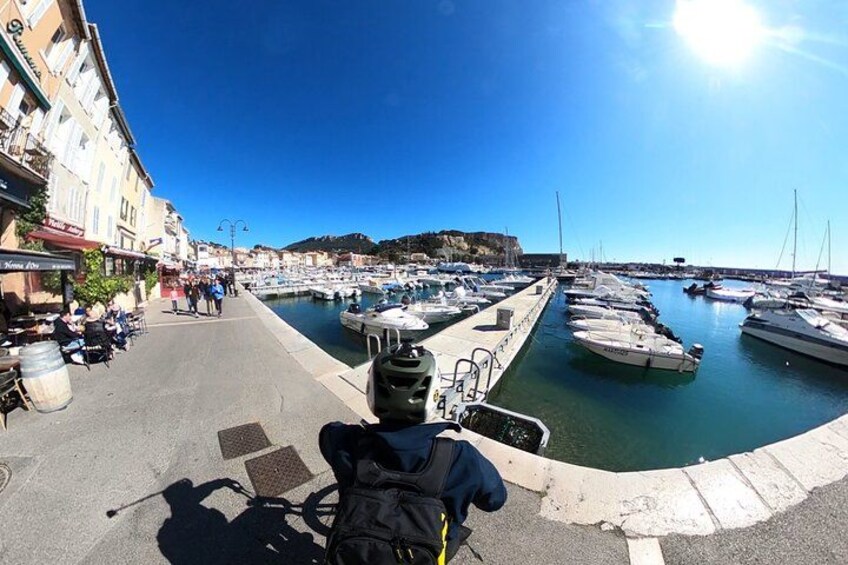 A person on a bicycle with a backpack, a marina with boats, and buildings along the waterfront. 4