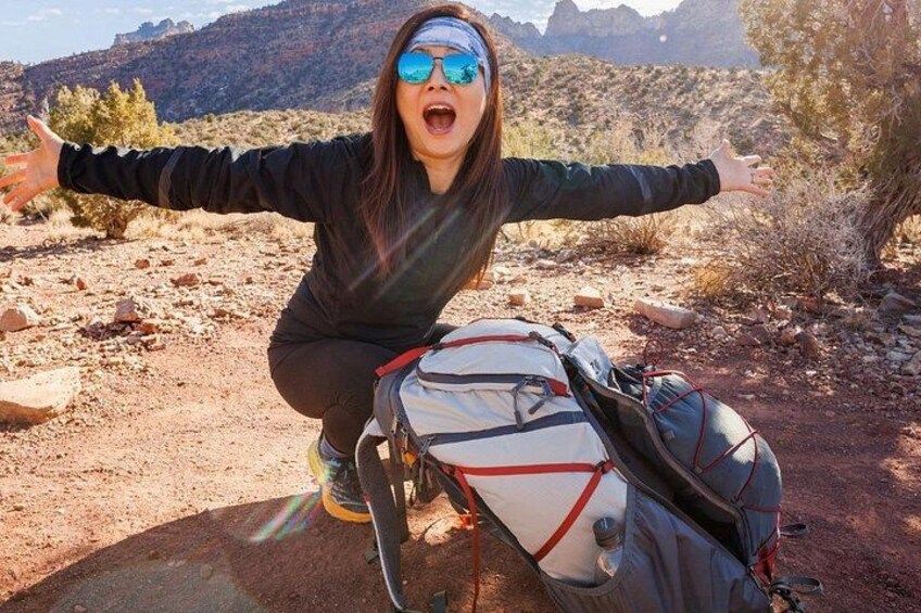 A person crouching on a rocky terrain with a backpack and a bicycle. 1