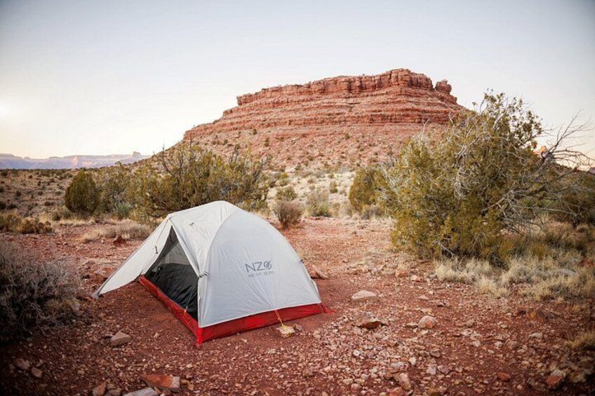 A tent in a desert landscape with red rock formations in the background. 2