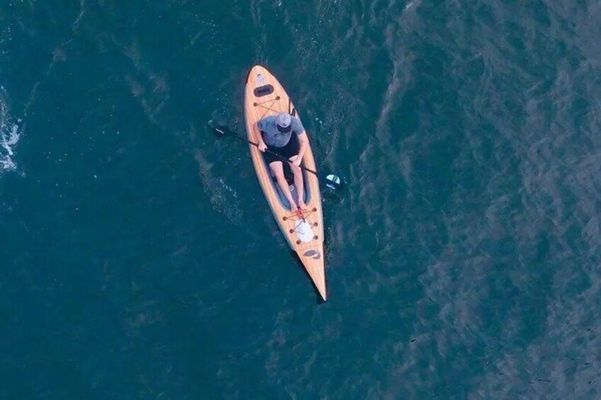 A single person paddling a wooden canoe on a body of water. 1