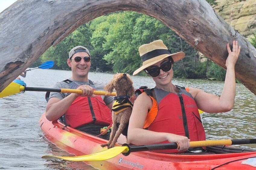 Two people in a kayak on a river, one holding a dog. 3
